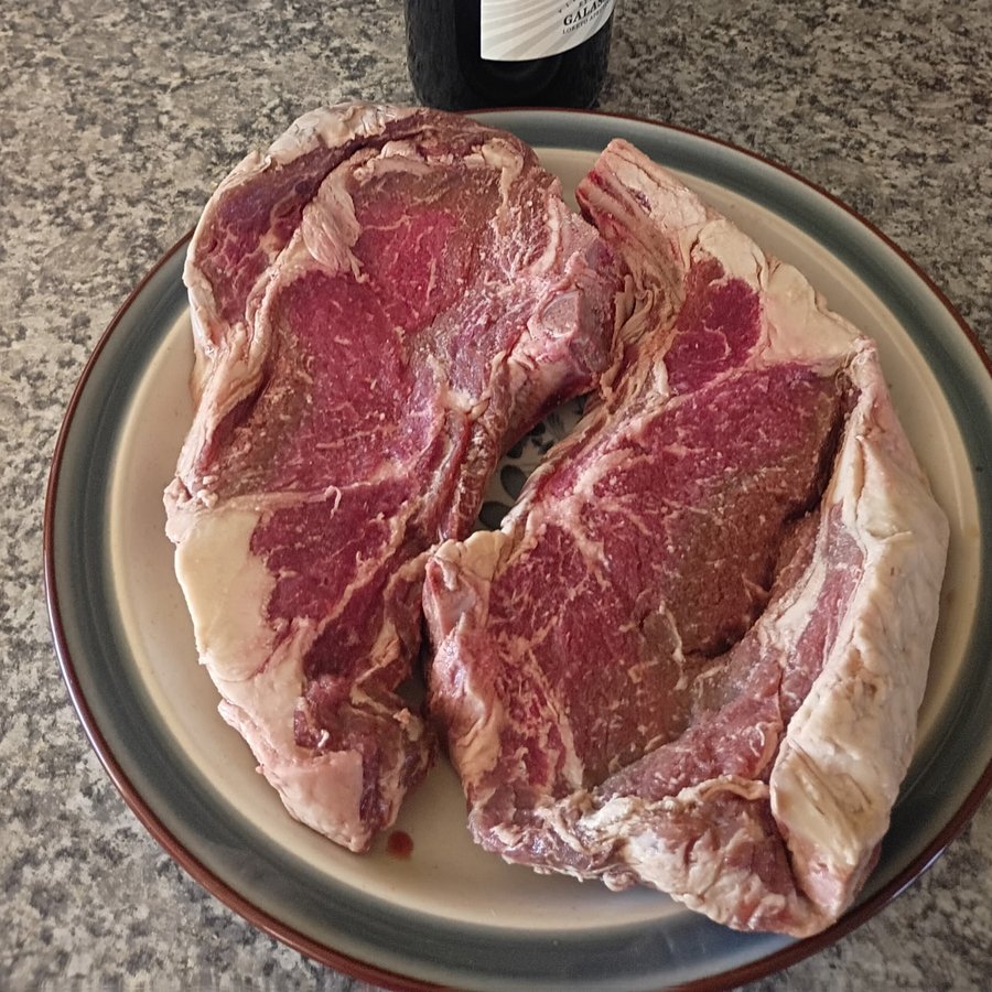 Fresh-cut steaks on a plate with a bottle of red wine